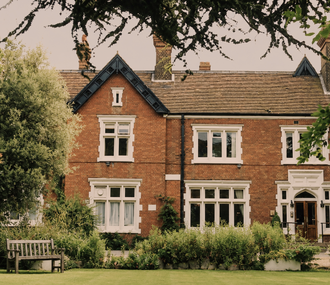 The exterior of The Holly Private Hospital, a low brick building set behind mature trees and a landscaped forecourt